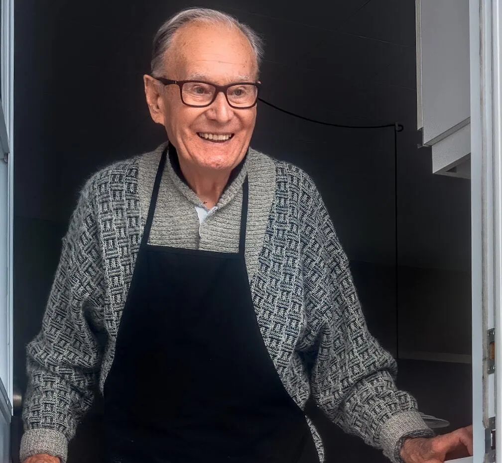 Man in black vest and black dress pants standing beside white wooden door