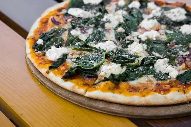Pizza with green leaves on brown wooden table