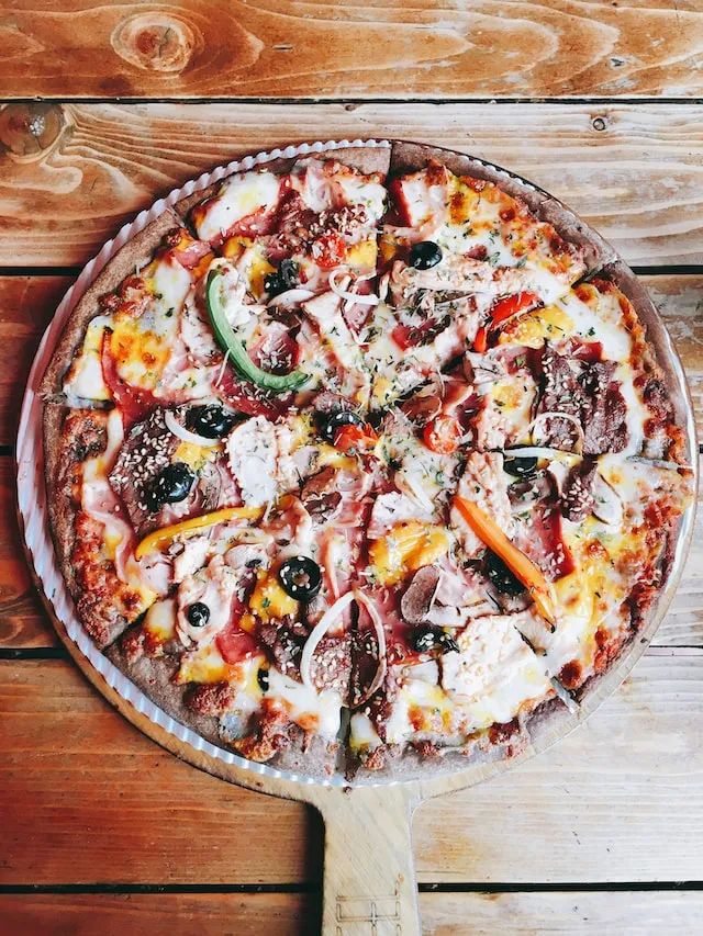 Pizza with green and red bell pepper and cheese on wood cutting board